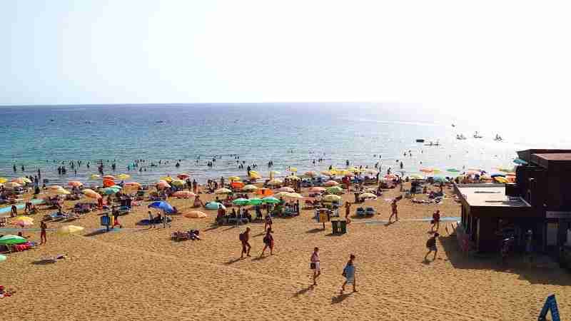 Ein gemütliches Café direkt am schönsten Sandstrand Maltas, der Golden Bay, mit Gästen, die maltesische Spezialitäten genießen.