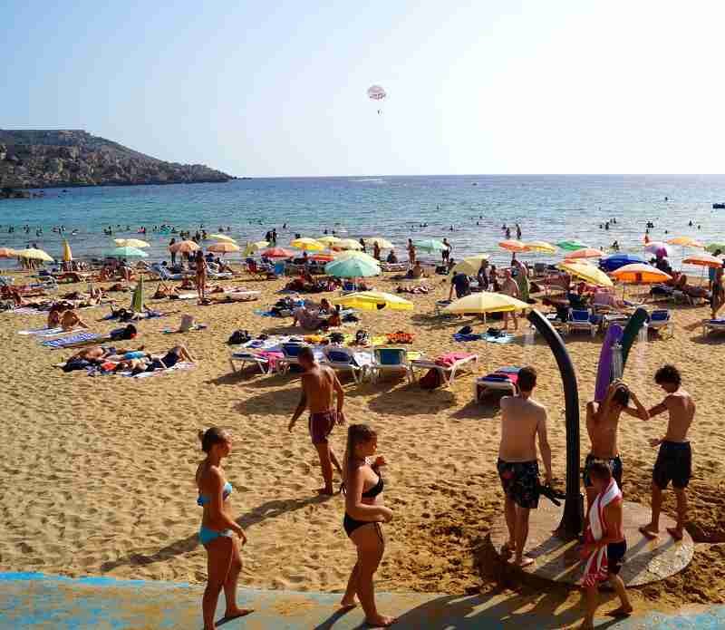 Familien genießen einen sonnigen Tag am schönsten Sandstrand Maltas, der Golden Bay, mit spielenden Kindern im flachen Wasser.
