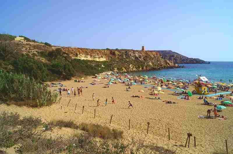 Golden Bay, der schönste Sandstrand Maltas, mit feinem goldenem Sand und kristallklarem türkisfarbenem Wasser, umgeben von grünen Hügeln.