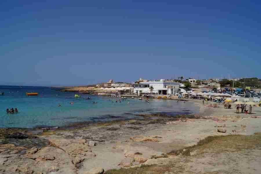 Sonnenanbeter entspannt unter Sonnenschirmen am Sandstrand von Little Armier Bay, während das Meer in der Sonne glitzert.