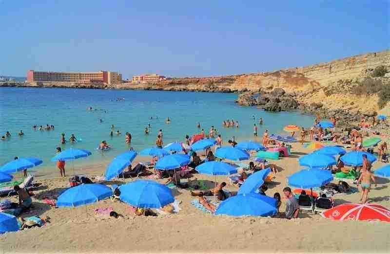 Sonnenanbeter entspannen unter Sonnenschirmen am flach abfallenden Sandstrand von Paradise Bay.