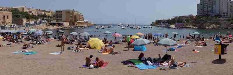 Panoramaaufnahme von St. George’s Bay – einer der vielseitigsten Strände auf Malta, umgeben von türkisblauem Wasser und malerischer Architektur.