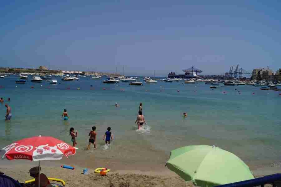 Einheimische erfrischen sich im klaren Wasser einer malerischen Bucht in Malta, während kleine Boote in der Nähe ankern.